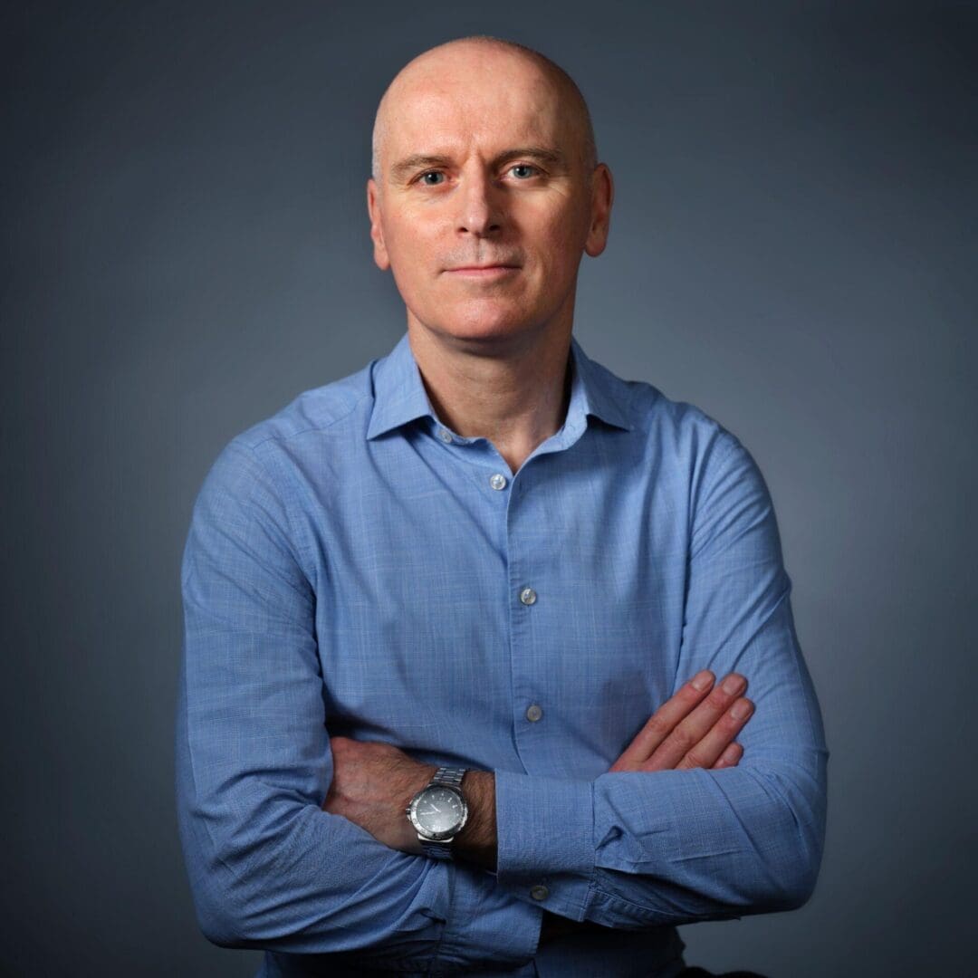 Bald man wearing blue shirt, arms crossed