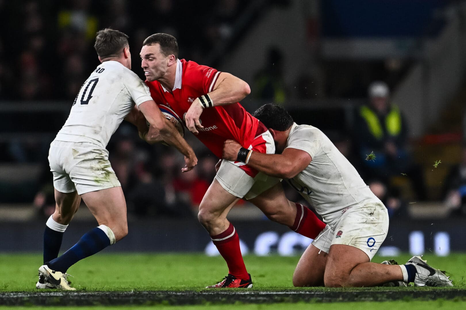 Rugby player in red tackled by two opponents