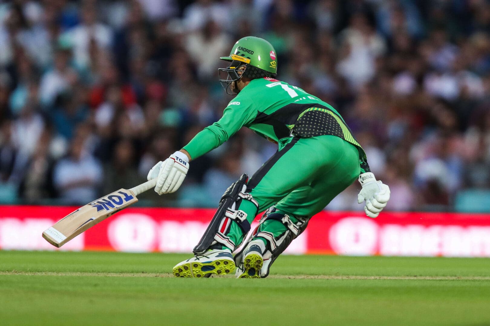 Cricket batsman in green sliding to play shot