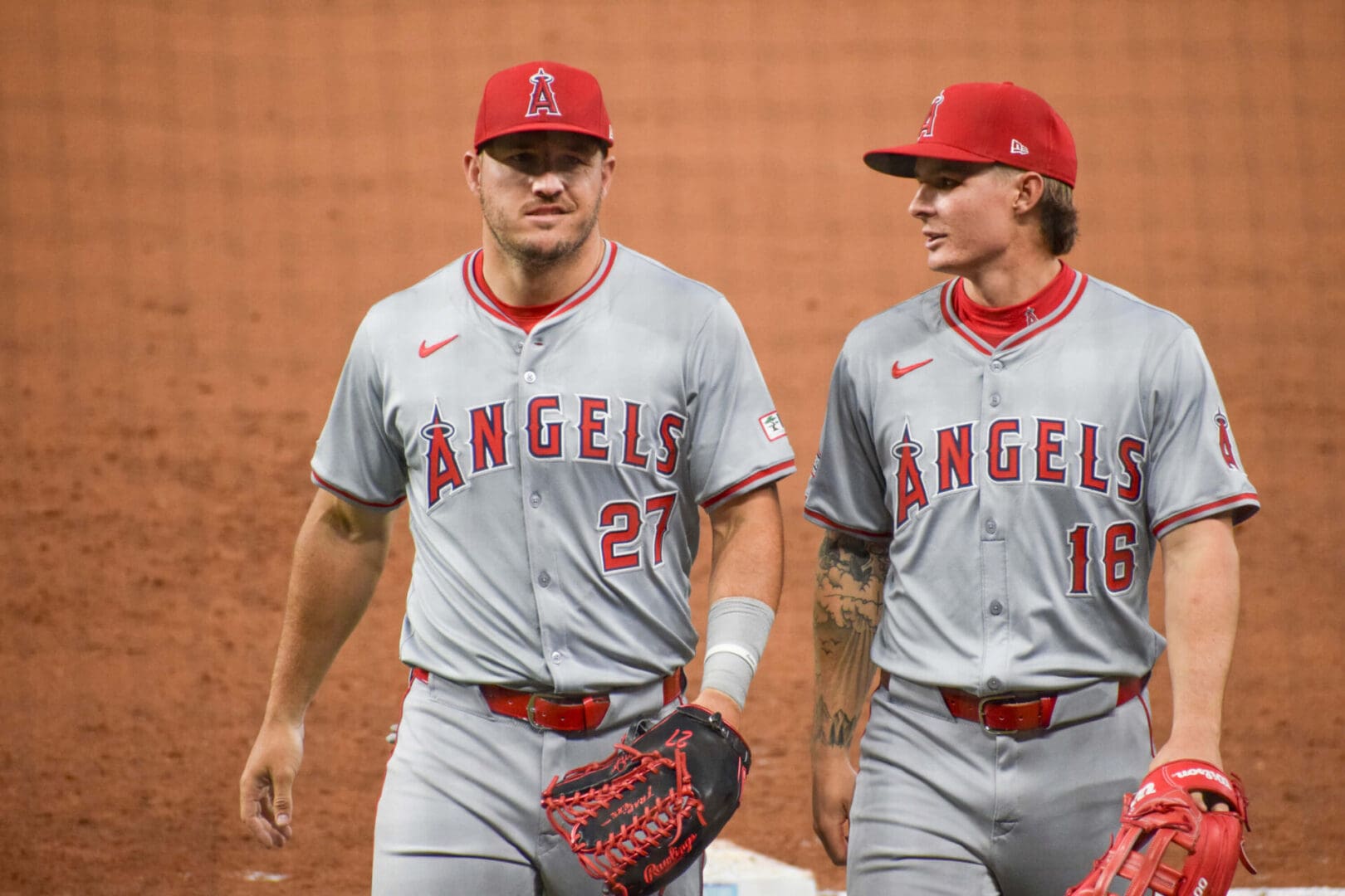 Two baseball players in grey uniforms are standing next to each other.