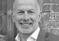 A man with bald head and white shirt smiling.