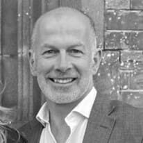 A man with bald head and white shirt smiling.
