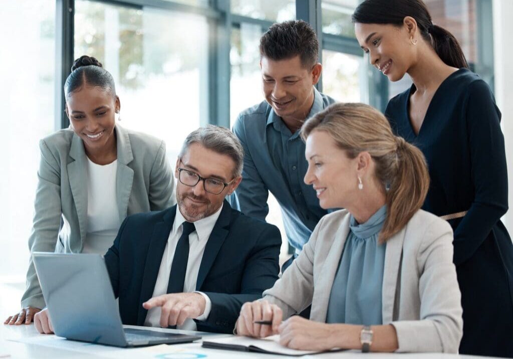 A group of people sitting around a table looking at a laptop.